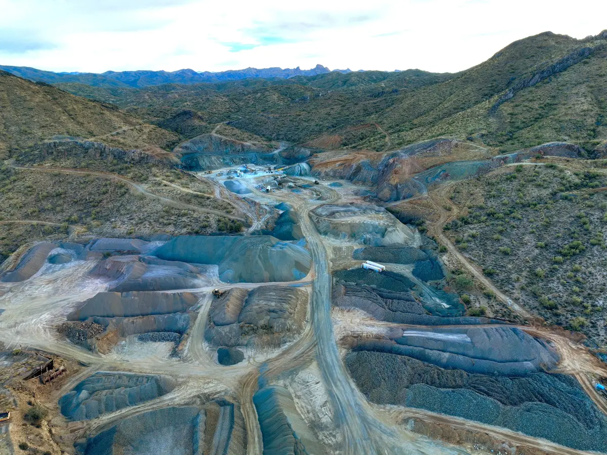 Aerial view of a terraced quarry in a desert valley, haul roads winding between blue-grey benches